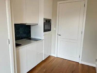 a white kitchen with white cabinets and a wooden floor at Appartement Huis ter Duinstraat in Noordwijk aan Zee