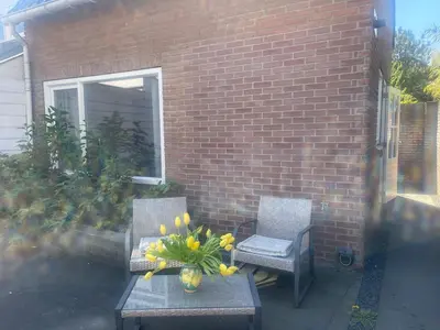 a patio with two chairs and a table with a vase of flowers at Wendy's Tiny Beachhouse in Noordwijk