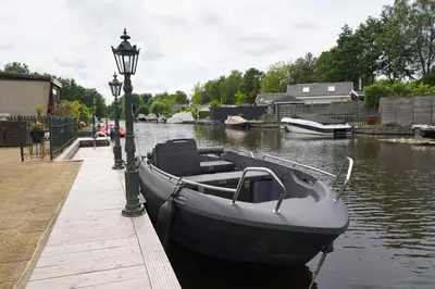 a boat tied to a dock next to a light pole at Chalet with waterfront sauna and boat in Loosdrecht