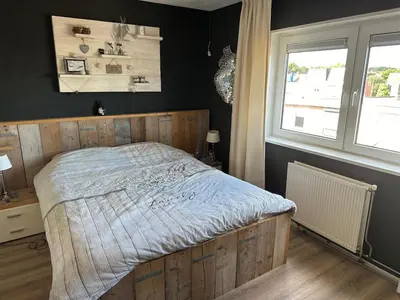 a bedroom with a bed with a wooden headboard and a window at Paleisje aan zee in IJmuiden