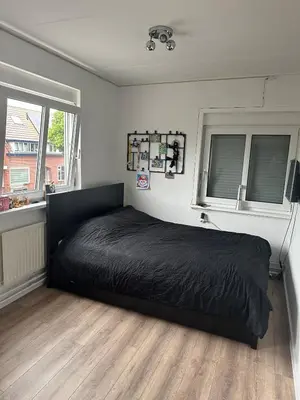 a bedroom with a black bed and two windows at Paleisje aan zee in IJmuiden
