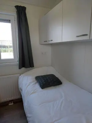 a small bedroom with a bed and a window at Recreatie aan de Vecht, chalet 3, genieten van de rust en ruimte en toch dichtbij de stad in Weesp