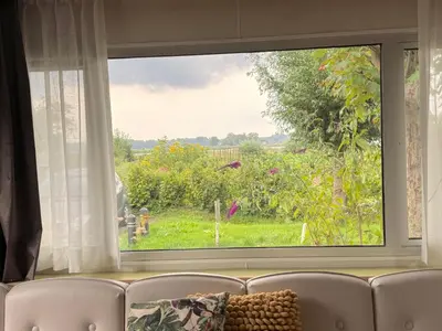 a window with a view of a garden from a couch at Vlinderzicht in Koedijk