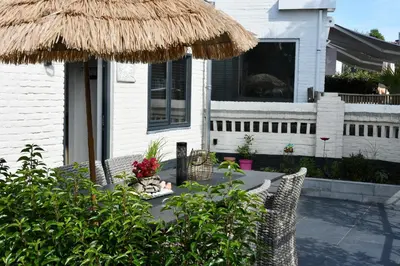 a patio with a table and a straw umbrella at Costa C en E in Noordwijk
