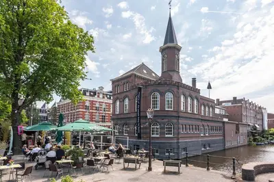a large brick building with a clock tower on a river at Panoramic canalview apartment in Amsterdam