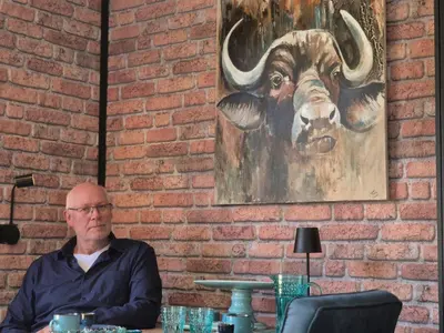 a man sitting at a table with a painting of a bull at B&B Aquamarijn Katwijk in Katwijk aan Zee