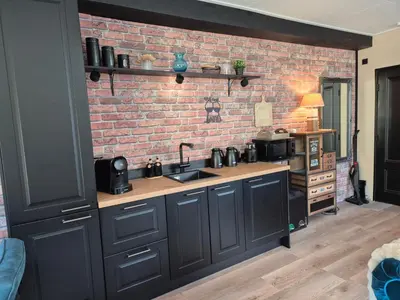 a kitchen with black cabinets and a brick wall at B&B Aquamarijn Katwijk in Katwijk aan Zee