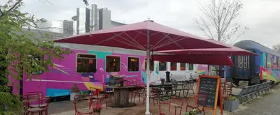 a purple tent with tables and chairs in front of a bus at Train Lodge Amsterdam in Amsterdam