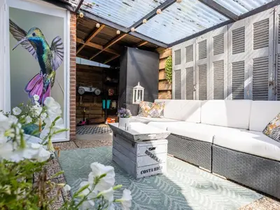 a patio with a white couch and a bird painting on the wall at Het Zonneschijnhuis in Dirkshorn