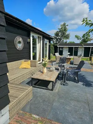 a patio with a wooden table and chairs and a table at De Fijne Blokhut in Nijkerkerveen