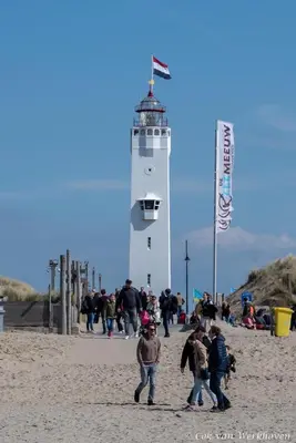 a group of people walking on the beach near a lighthouse at Bulbs & Beach in Noordwijk