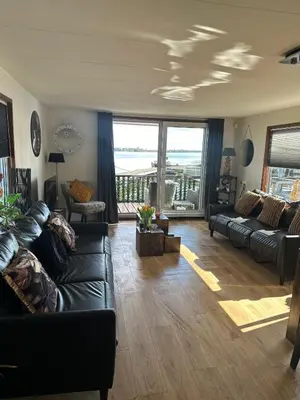 a living room with a black leather couch and a balcony at Woonboot De Witte loosdrechtse plassen in Loosdrecht