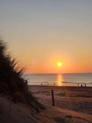 a sunset on the beach with people walking on the beach at Studio 21 stylish and luxurious apartment in Noordwijk