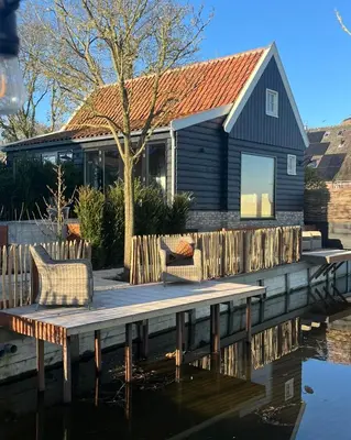 a wooden dock with two chairs and a house at B&B De Wilgenhoeve in Kwadijk