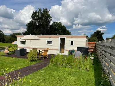 a caravan in a garden with a table and an umbrella at Houseboatvinkeveen Lelie in Vinkeveen