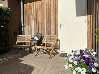 two chairs and a table on a patio with flowers at Appartement Buissant des Amorie! in Castricum