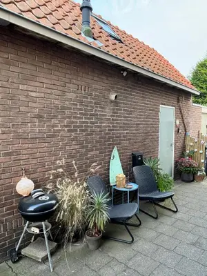 a brick building with three chairs and a table with a surfboard at Tiny House - Surfers Paradise in Noordwijk