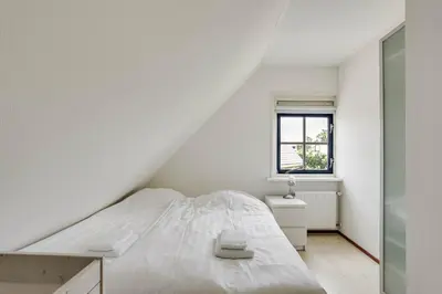 a white bedroom with a bed and a window at Vakantiepark Schoorlse Duinen in Schoorl