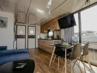 a living room and kitchen with a table and chairs at Houseboat at Marina with Lake Views in Uitgeest