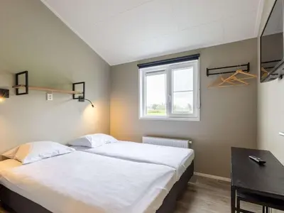 a bedroom with a bed and a desk and a window at Karper Vakantiepark De Groote Vliet in Wervershoof