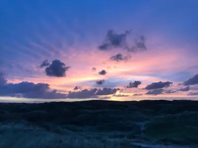 a sunset over a field of rolling hills at Kust 3 in Egmond aan Zee