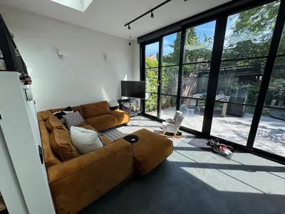 a living room with a brown couch and a large window at Family home Amsterdam Zuid - South in Amsterdam