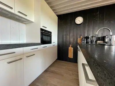 a kitchen with white cabinets and a clock on the wall at De Tuinkamer in Egmond aan den Hoef