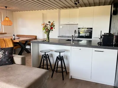 a kitchen with white cabinets and a counter with stools at De Tuinkamer in Egmond aan den Hoef