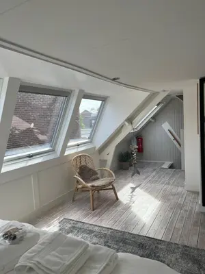 a attic room with a chair and two windows at Zeemeeuw aan Zee in Egmond aan Zee