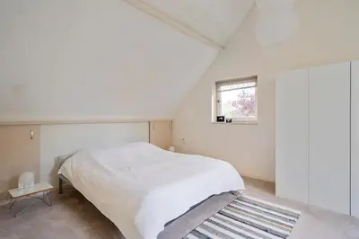 a white bedroom with a bed and a window at The Green Oasis charming family villa with garden and private parking in Zandvoort