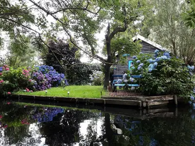a garden with flowers and a house next to a pond at Hortensia Eiland in Zegveld