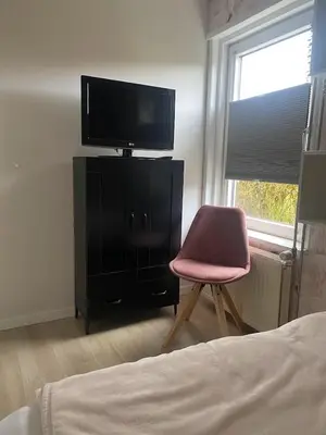 a bedroom with a chair and a television on a dresser at Delightful tropical retreat close to the sea in Warmenhuizen
