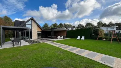 a house with a green yard with two chairs at Villa Liferla - Wellness met sauna en jacuzzi in Zeewolde
