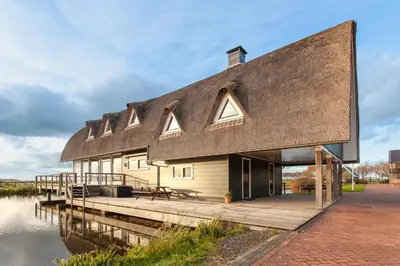 a house with a thatched roof on the water at 10P 4B Luxe Villa with Pool and Sauna in Spijkerboor in Spijkerboor