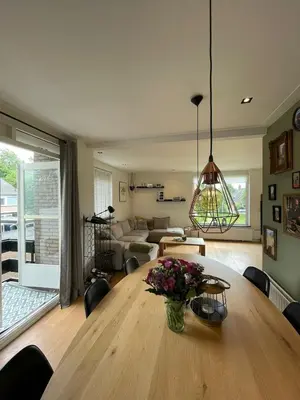a living room with a wooden table with a vase of flowers at Prachtige, lichte condo met balkon in Bergen