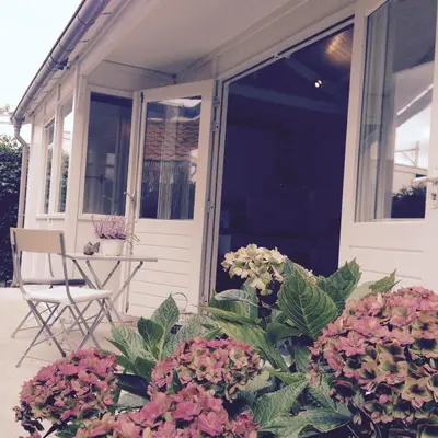 a porch with flowers and a chair on it at Tiny House Madame Jeanette nabij centrum en zee in Zandvoort