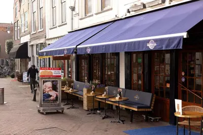 a restaurant with tables and a blue awning on a street at Elegant City Apartment in the Heart of Gouda in Gouda