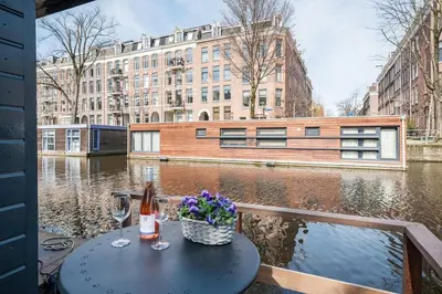 a table with a glass of wine and flowers on a canal at Luxury Houseboat-Apartment Lady Jane in Amsterdam