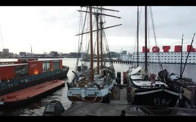 three boats docked at a dock with a cruise ship at The Vega 1909 - Historic Wooden Ship in Amsterdam