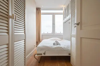 a small bedroom with a bed and a window at Sandhues Beachfront Apartment in Zandvoort