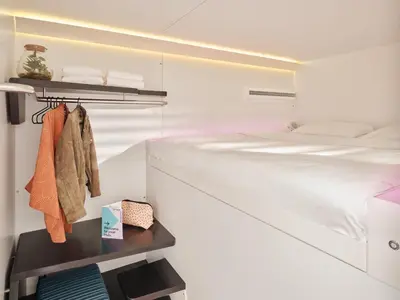 a white bedroom with a bed and a shelf at CityHub Amsterdam in Amsterdam