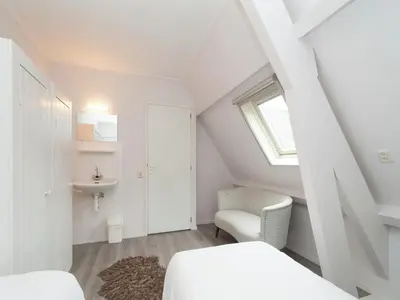 a attic bedroom with a bed and a chair at Dune Top Family Retreat in Bergen aan Zee
