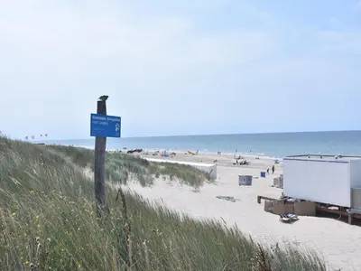 a beach with a blue sign and people on the beach at Dune Top Family Retreat in Bergen aan Zee