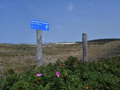 a fence with a blue sign next to some flowers at Dune Top Family Retreat in Bergen aan Zee