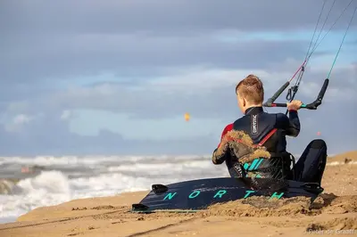 a man sitting on the beach holding onto a kite at Beautiful loft in Katwijk aan Zee in Katwijk aan Zee