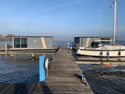 a dock with a house and a boat on the water at Houseboat Uitgeest in Uitgeest