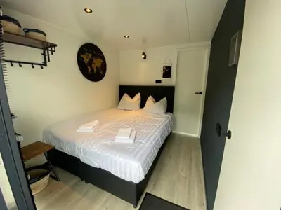 a bedroom with a bed with white sheets and a clock at Houseboat Plus Uitgeest in Uitgeest