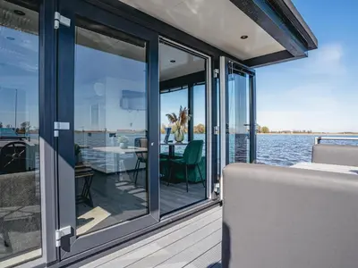 a balcony with glass doors and a table on a boat at Houseboat Plus Uitgeest in Uitgeest