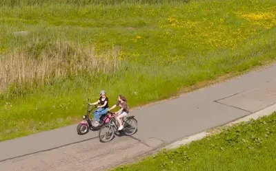 two women riding bikes on a road next to a field at Houseboat Woude Uitgeest in Uitgeest