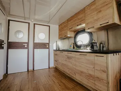 a kitchen with wooden cabinets and a sink and a door at Houseboat Campi Uitgeest in Uitgeest
